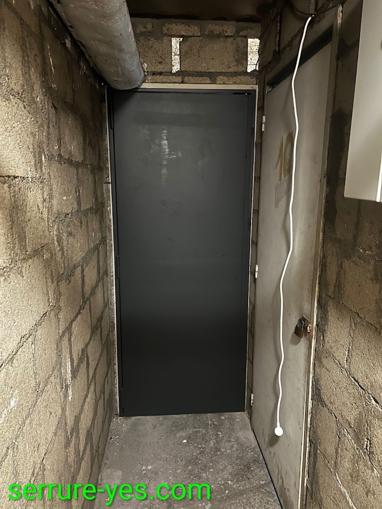 Porte de cave blindée métallique de teinte sombre installée dans un sous-sol en parpaings