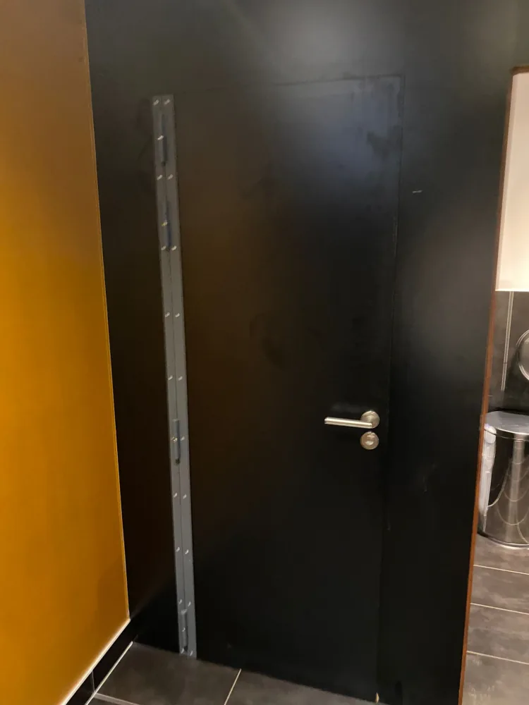 Barre de pivot en acier galvanisé présentée le long du montant d'une porte noire avant fixation