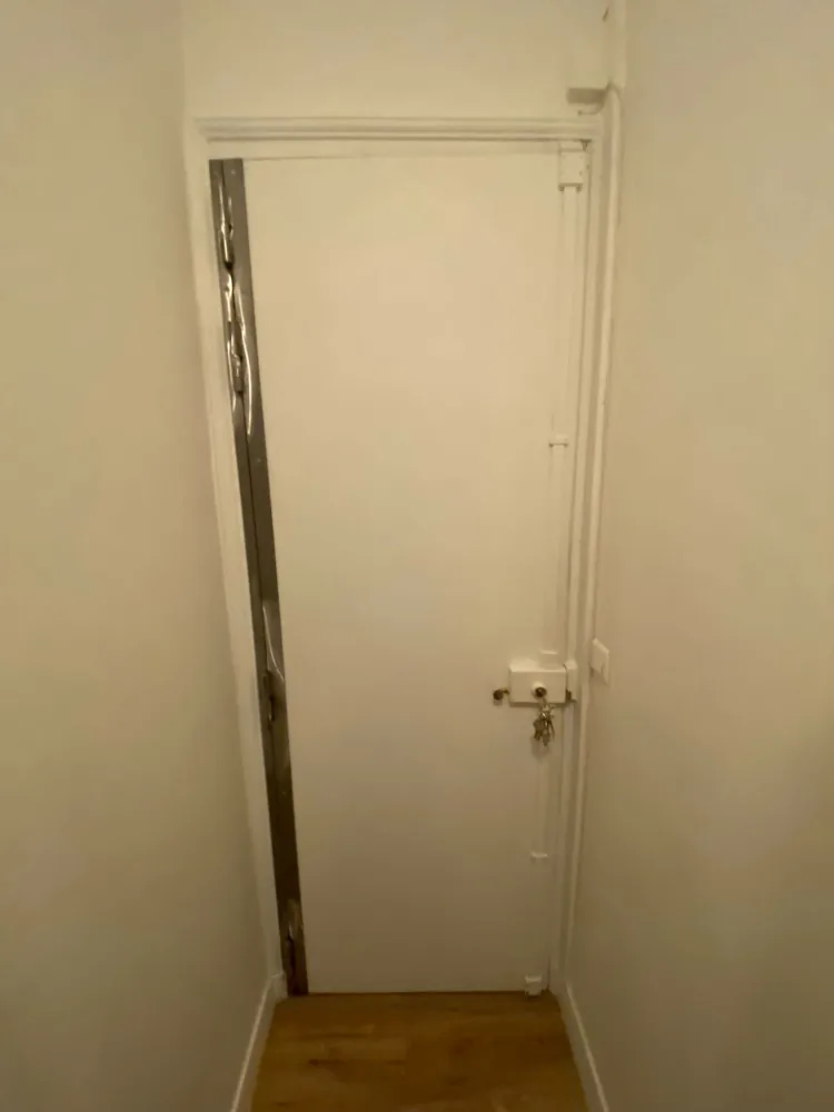 Barre de pivot en acier posée côté paumelles d'une porte blindée blanche, serrure apparente côté opposé
