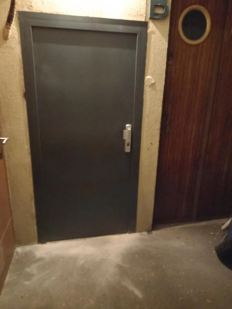 Porte métallique anthracite d'accès parking avec plaque de propreté et cylindre, dans un sous-sol