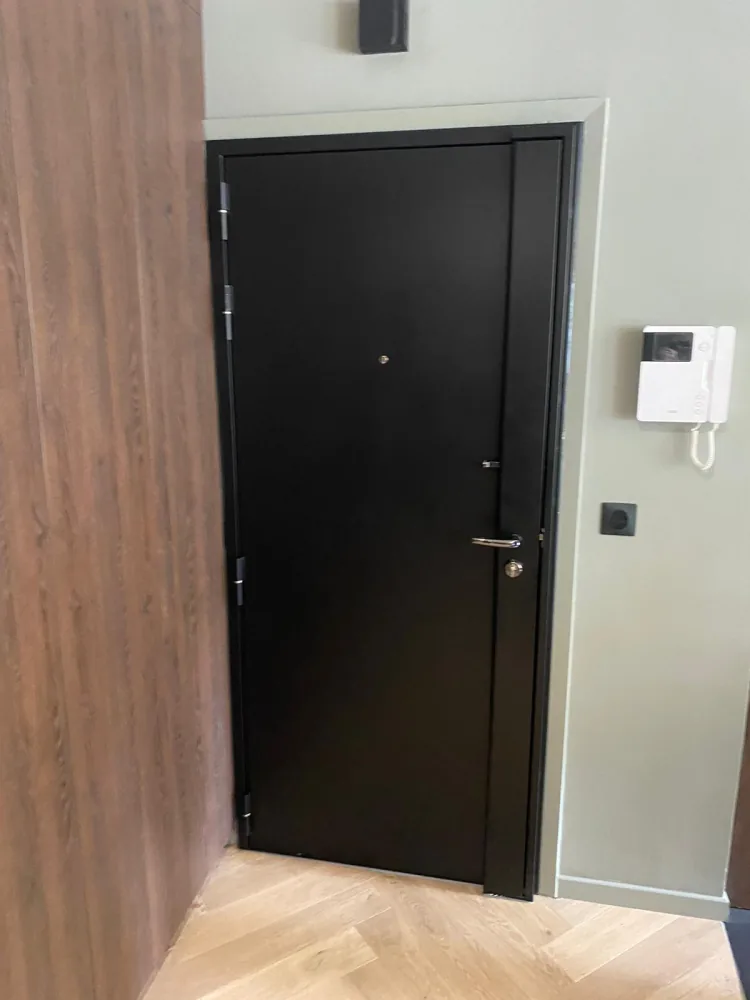 Porte blindée noire avec carénage noir, béquille chromée et interphone vidéo dans une entrée moderne